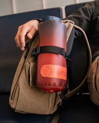 A Rumpl travel blanket attached to the side of a backpack.